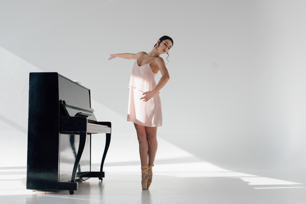 young ballerina dancing in sunlight near black piano  - Photo, Image