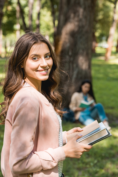 selective focus of cheerful girl holding books with friend on background - Photo, Image