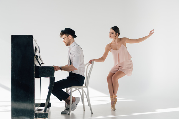 handsome musician playing piano while beautiful ballerina dancing near chair - Photo, image
