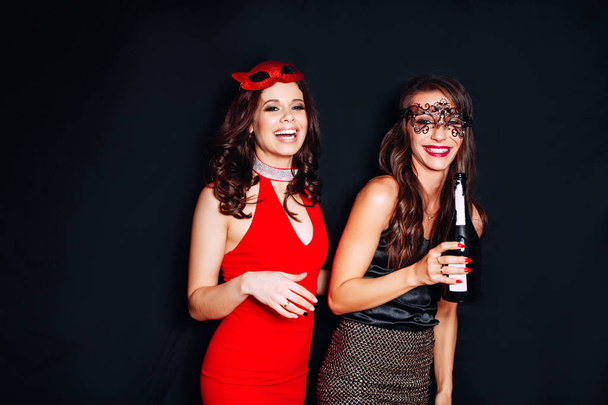 Cute girls, cheerful best friends, sisters enjoying party, having fun, hugging with glasses of wine. Wearing bright dresses with spangles - Foto, Imagem