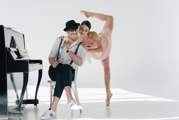 hezký muzikant sedí na židli s rostl, zatímco mladá baletka tanec nablízku  - Fotografie, Obrázek