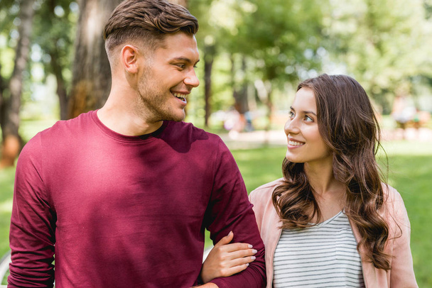 cheerful couple looking at each other while smiling in park - Фото, изображение
