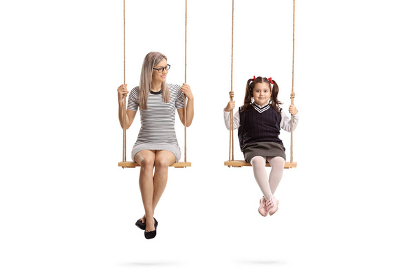 Full length portrait of a young woman and little schoolgirl sitting on swing isolated on white background - Zdjęcie, obraz