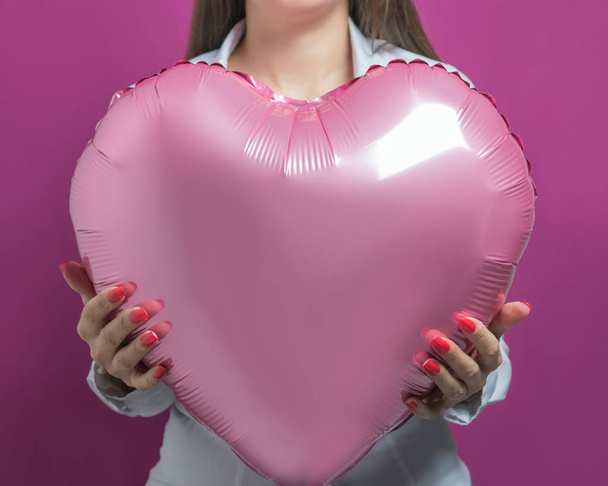 Young pretty woman holding a heart shaped air balloon. Valentine's day concept. - Photo, Image