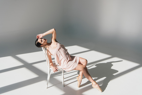 日光の白い椅子に座って美しい若いバレリーナ  - 写真・画像