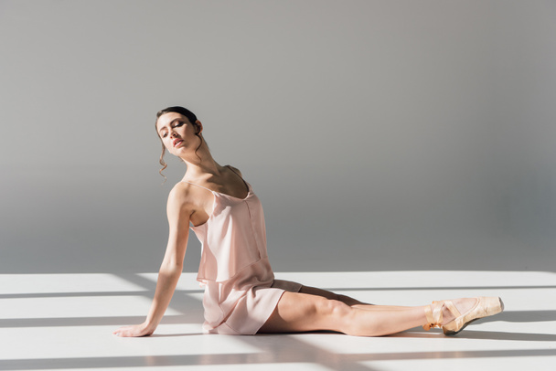 young ballerina in pink dress sitting on floor in sunlight  - Фото, изображение