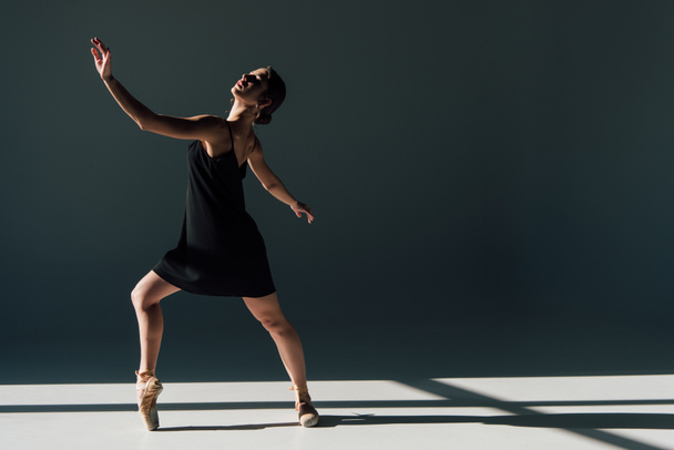 красивая молодая балерина в черном платье танцует на солнце
  - Фото, изображение