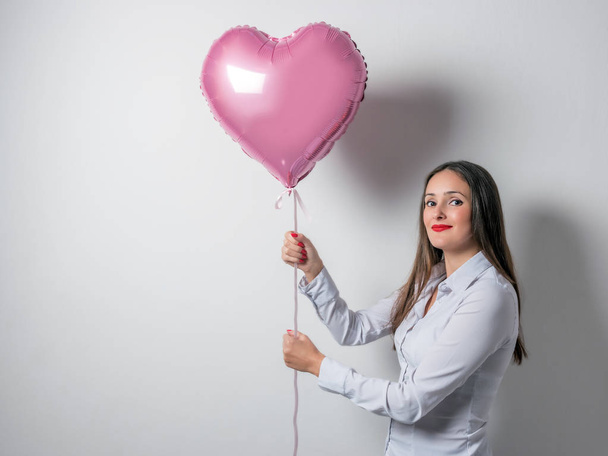 Beautiful young woman with a heart shaped balloon on a bright background. Valentine's day concept. - Foto, afbeelding