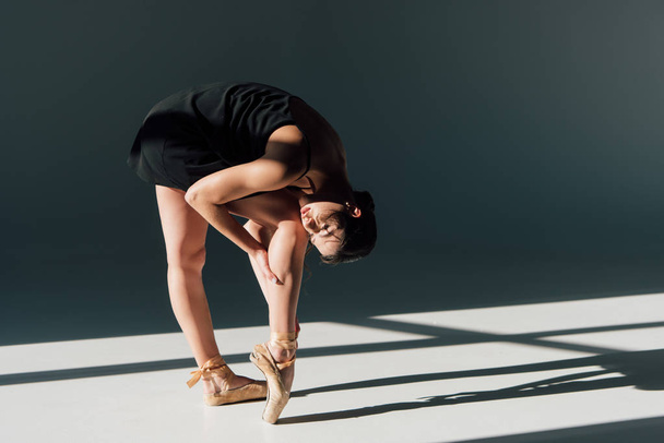 bailarina jovem em vestido preto que se estende na luz solar
 - Foto, Imagem