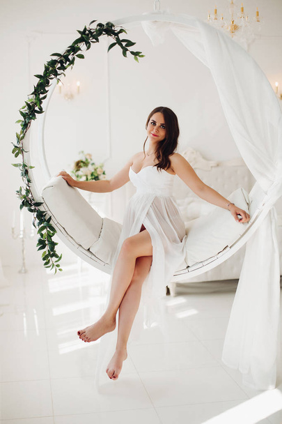 Gorgeous pregnant woman in white gown on designed chair. - Fotografie, Obrázek