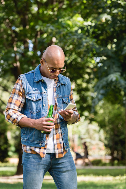 bonito afro-americano homem olhando para smartphone enquanto segurando garrafa
  - Foto, Imagem
