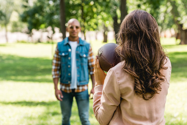 selective focus of girl holding american football and looking at african american boyfriend - Foto, Imagem