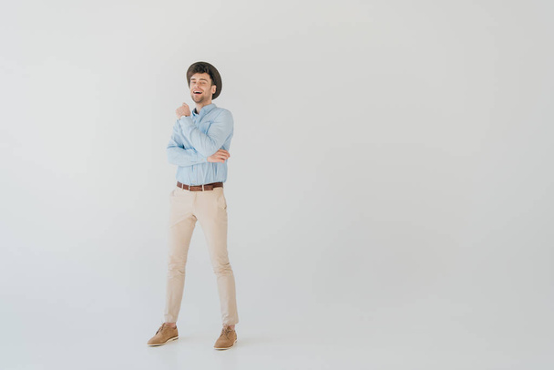 handsome smiling man in blue shirt and beige jeans isolated on grey - Foto, afbeelding