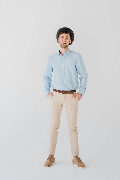 handsome cheerful man in blue shirt and beige jeans isolated on grey - Foto, Imagen
