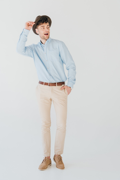 happy handsome man in blue shirt and beige jeans with hand in pocket isolated on grey - Foto, Imagem