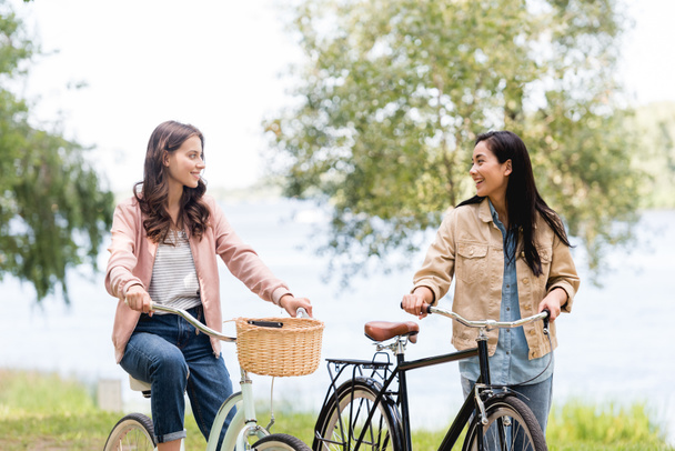 cheerful girls riding bicycles and smiling in park  - Fotoğraf, Görsel