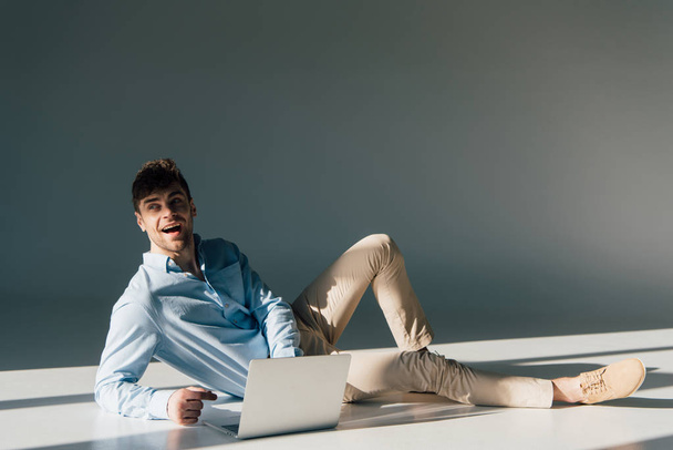 веселий красивий чоловік використовує ноутбук, сидячи на сонячному світлі
 - Фото, зображення