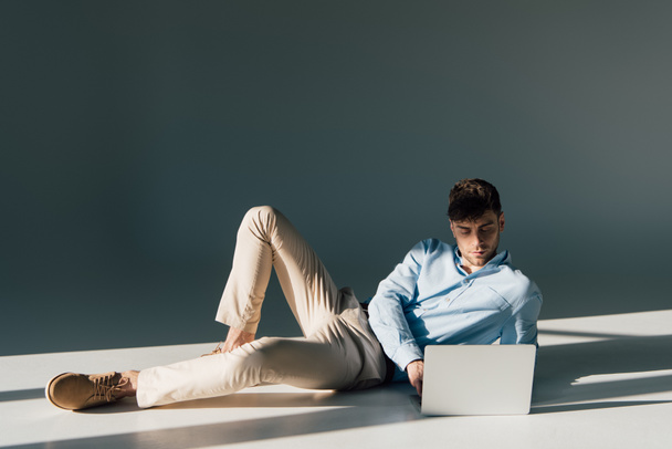 handsome man using laptop while lying in sunlight  - Фото, изображение