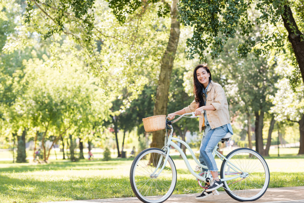 happy pretty girl smiling while riding bicycle in park  - Zdjęcie, obraz