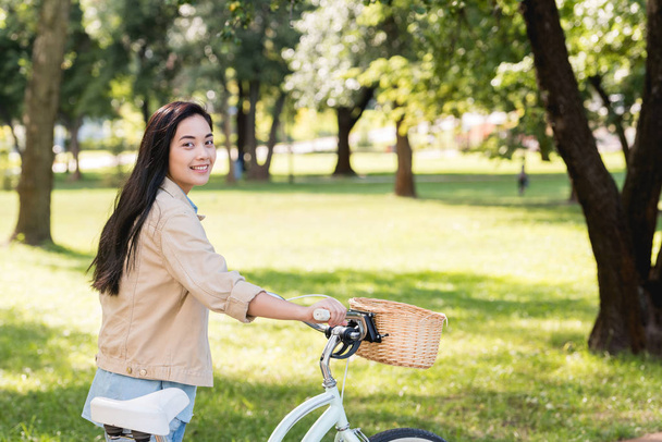 cheerful pretty girl smiling while riding bicycle in park  - Valokuva, kuva