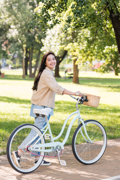 cheerful young woman smiling while riding bicycle in park  - Foto, afbeelding