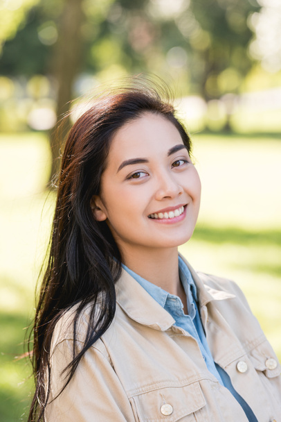 attractive young woman smiling while looking at camera in park - Photo, Image