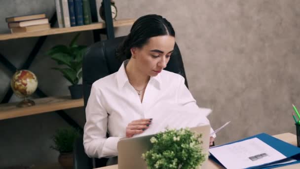 Young female is looking at paperwork at his desk in office - Séquence, vidéo