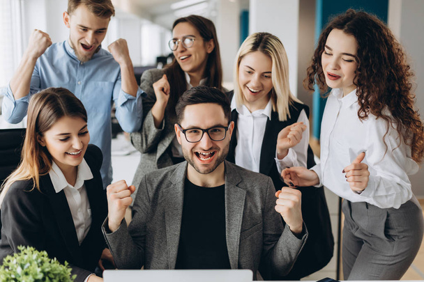Jovens empresários bem-sucedidos estão levantando as mãos em punhos e gritando de felicidade enquanto trabalham com um computador no centro de negócios
 - Foto, Imagem