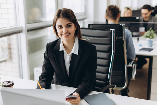 Porträt einer glücklichen Geschäftsfrau, die an ihrem Arbeitsplatz im Büro sitzt - Foto, Bild