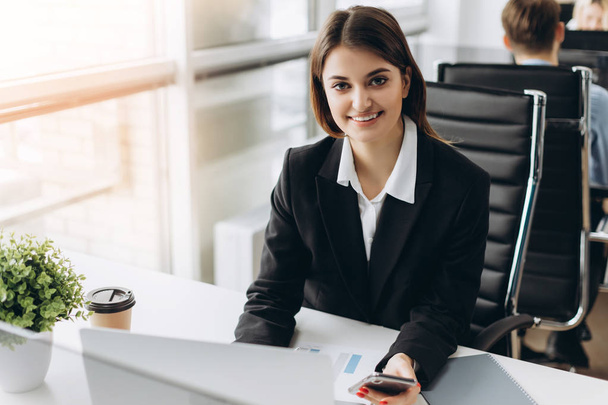 Beautiful young and successful smiling girl sits at the table in her office. Businesswoman - Фото, зображення