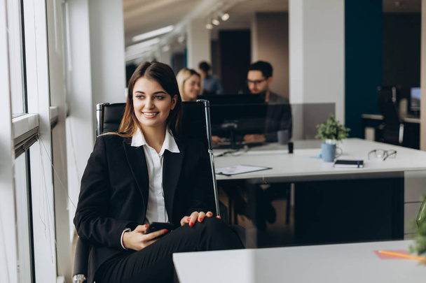 Smiling business woman using cell phone with colleagues on background in office. - Photo, Image