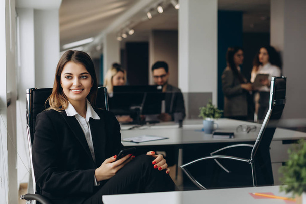 Smiling business woman using cell phone with colleagues on background in office. - Fotoğraf, Görsel