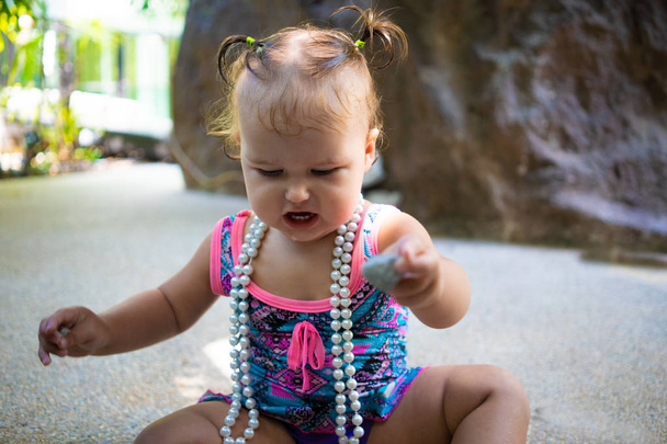 une fille en maillot de bain avec des perles blanches est surprise, se réjouit, crie, lève les mains. concept de mode pour enfants
. - Photo, image
