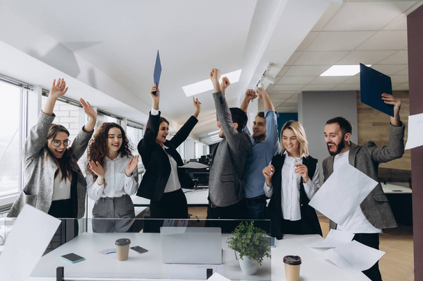 Picture of happy business team celebrating victory in office. Successful business team throws pieces of paper in modern office. - Fotó, kép