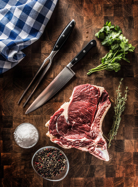 Rib eye steak with bone on butcher board with herbs salt pepper fork and knife - Valokuva, kuva