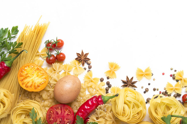 Verschillende soorten Italiaanse pasta, nesten, spaghetti, specerijen, Red hot chili peper, kippeneieren, tomaten, cherry, lichte witte stenen achtergrond. Plat lag, top uitzicht - Foto, afbeelding