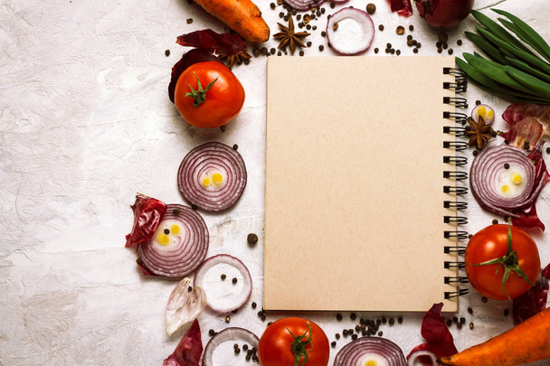 Φρέσκα λαχανικά γύρω από το σημειωματάριο για τις συνταγές τροφίμων σε ανοιχτόχρωμο φόντο. Η ιδέα του μαγειρέματος, χορτοφαγία και υγιεινή διατροφή - Φωτογραφία, εικόνα