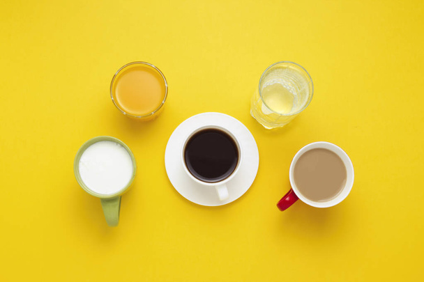 Group of Drinks in Multicolored Cups, Black Coffee, Coffee with Milk, Yogurt, Just Water, Orange Juice on Yellow Background. Flat lay, top view - Foto, afbeelding