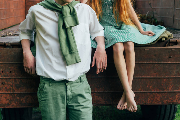unrequited first love. a barefooted girl in a green dress sits on the back of a car and hugs a barefoot, next to a standing guy, a summer day in the village. teenagers in the village. rural life of ad - Foto, Bild