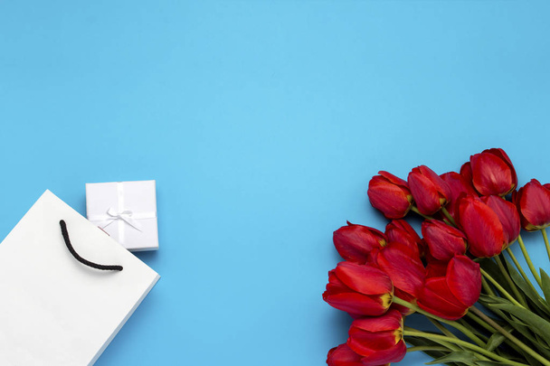 Sac cadeau blanc, une petite boîte cadeau blanche et un bouquet de tulipes rouges sur fond bleu. Concept Offre un fiançailles ou mariage, shopping
 - Photo, image