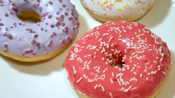 Close-up van video van drie donuts met kleurrijke hagelslag op witte plaat. - Video