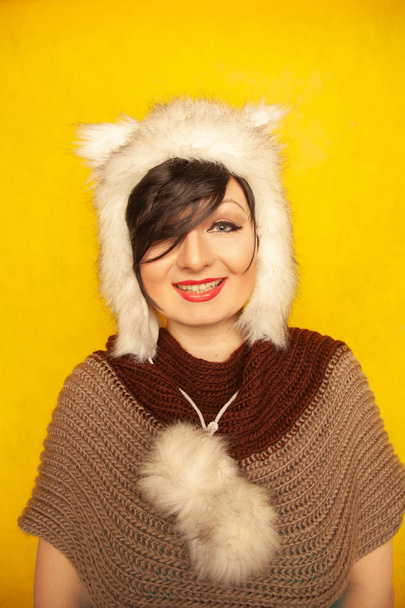 charming caucasian girl in a fur white hat with cat ears smiles and enjoys life on a yellow solid background in the Studio alone - Fotoğraf, Görsel