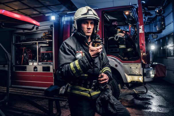 Tűzoltó, védelmi egyenruhában, mellette egy tűzoltóautó, és beszélt a rádióban. A tűzoltókat az éjszakai megérkezett - Fotó, kép