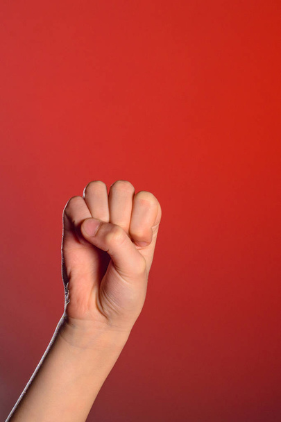Mão humana que apertou os dedos em um punho, simbolizando ódio e resistência, isolado em um fundo vermelho
 - Foto, Imagem