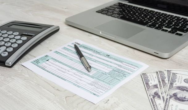US tax form next to computer laptop, dollar bills, calculator and tax form 1040. tax form us business income office hand fill concept - Φωτογραφία, εικόνα