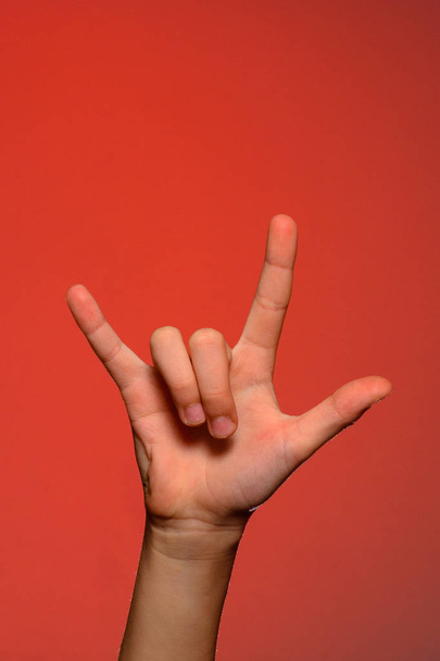 Mão humana mostrando três dedos, simbolizando estilo rock, isolado em um fundo vermelho
 - Foto, Imagem