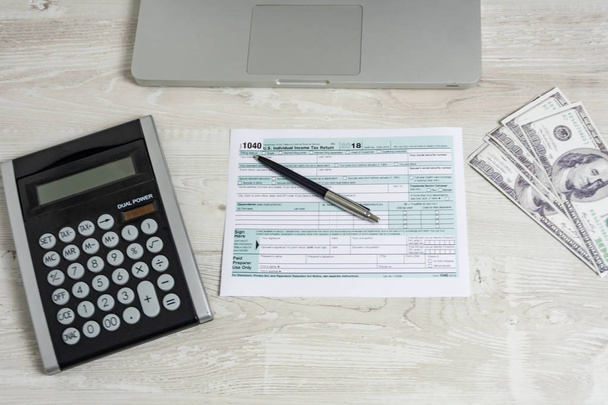 Formulário de imposto dos EUA ao lado de laptop de computador, notas de dólar, calculadora e formulário de imposto 1040. conceito de preenchimento de mão escritório de renda de negócios
 - Foto, Imagem