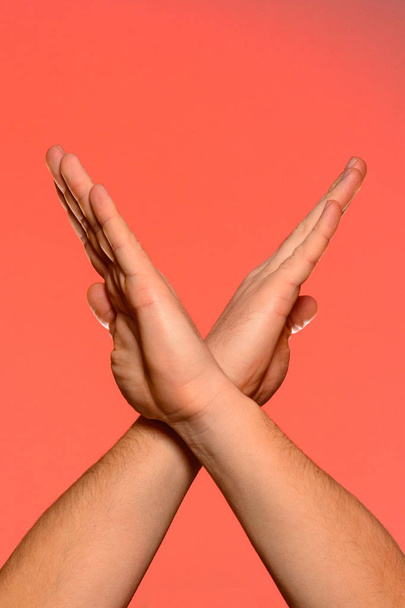 Human hands folded crosswise, which symbolize the wings of a bird or the sign of xx, isolated on a red background - Foto, Imagem