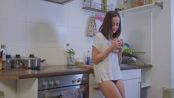 Tired girl in underwear drinks breakfast tea in the kitchen - 写真・画像