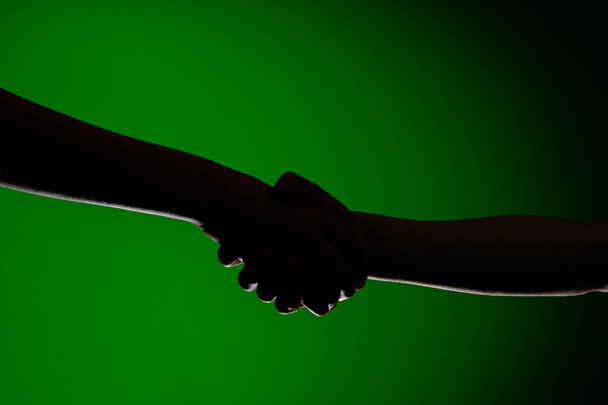 Two hands handshake, isolated on a green background, symbolizing friendship and reconciliation - Photo, Image